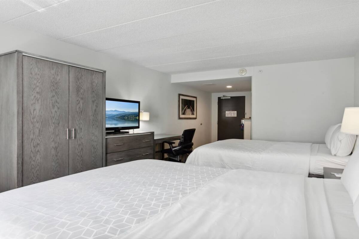 A hotel room with two beds, a desk with a TV, a wardrobe, and a door leading to another room.