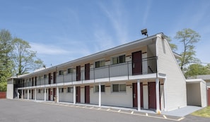A two-story motel with a balcony on the second floor, a parking lot in front, and a clear sky. - Red Roof Inn Neptune - Jersey Shore (Neptune City)