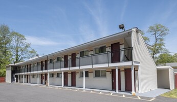 Un motel à deux étages, doté d’un balcon au deuxième étage, d’un parking à l’avant et offrant une vue sur un ciel dégagé.