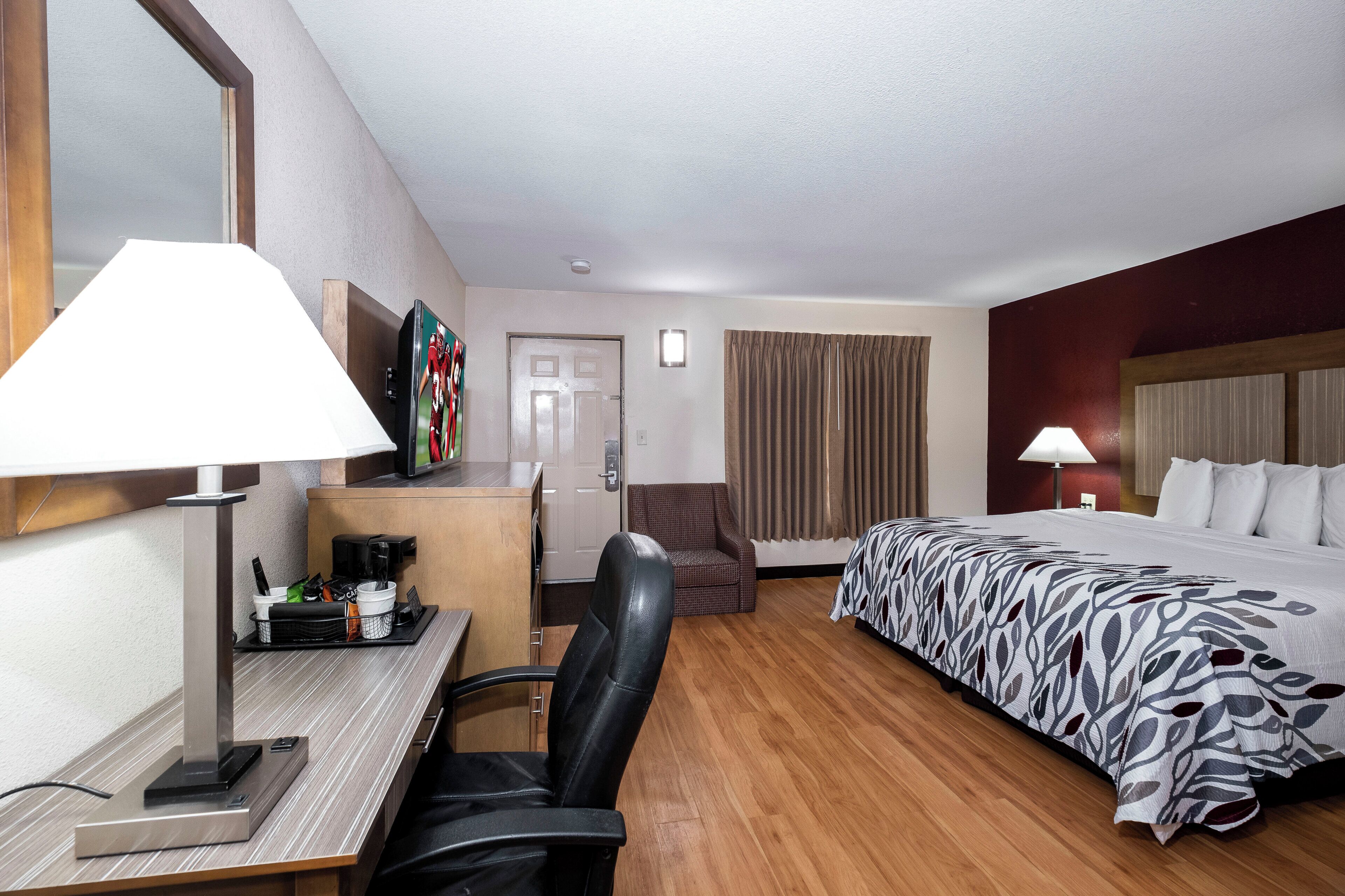 Une chambre d’hôtel comprenant un lit, un bureau avec une machine à café, une chaise, un téléviseur et une fenêtre avec des rideaux.