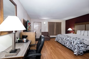 Une chambre d’hôtel comprenant un lit, un bureau avec une machine à café, une chaise, un téléviseur et une fenêtre avec des rideaux.