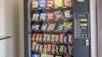 A vending machine with snacks and drinks, including brands like Doritos and Lay's, and a push button for operation.