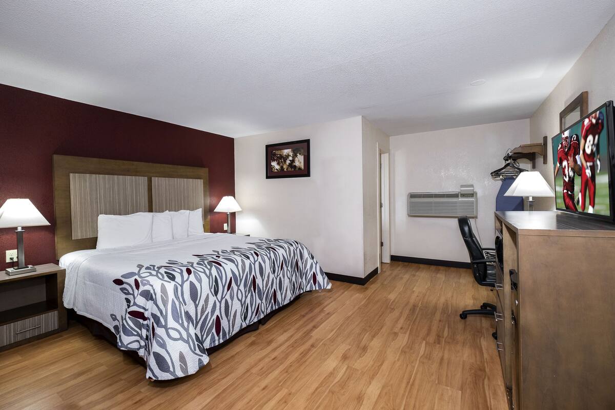 Ein Hotelzimmer mit einem Bett, zwei Nachttischlampen, einem Schreibtisch mit Lampe, einem Kleiderschrank und einem Fernseher auf einem Tisch.