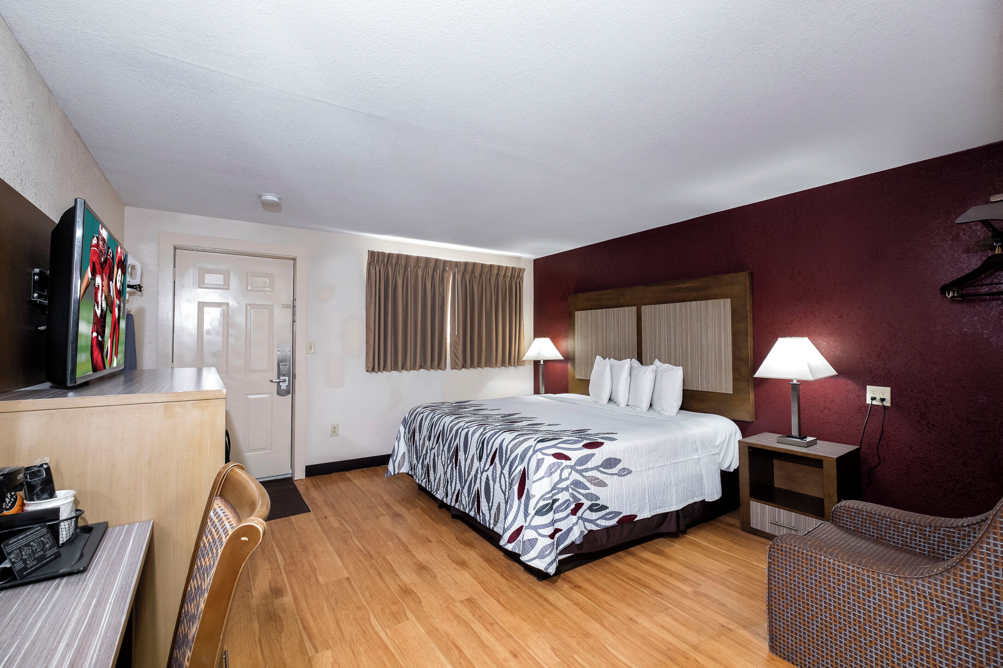 A hotel room with a bed, a desk, a television, and a chair.