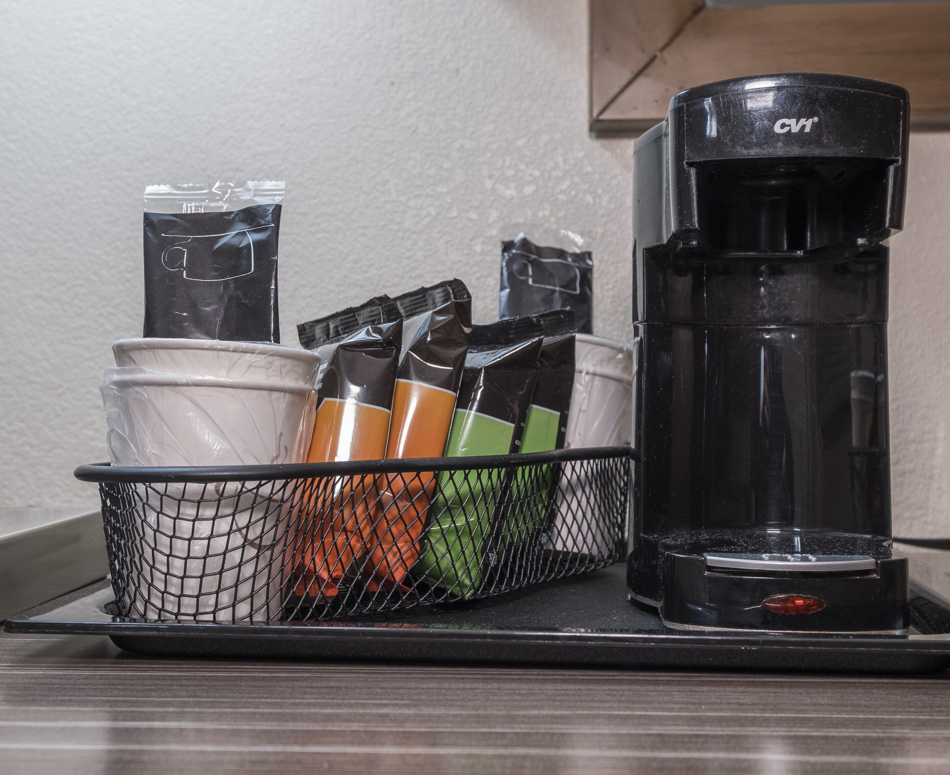 A coffee maker and a basket with coffee pods and a cup on a countertop.