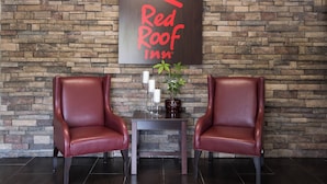 A Red Roof Inn sign on a stone wall, two leather chairs, a small table with candles and a potted plant. - Red Roof Inn Neptune - Jersey Shore (Neptune City)