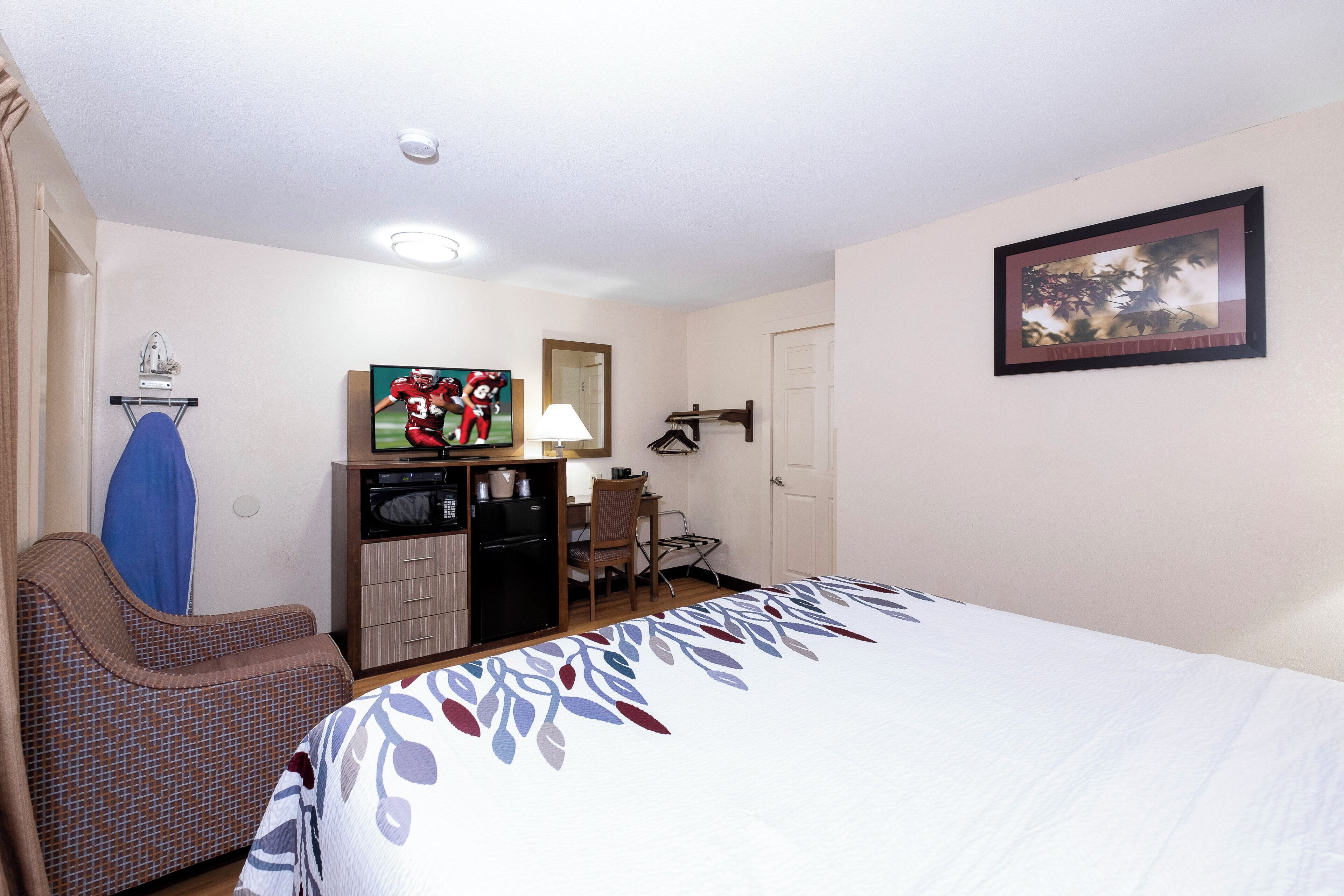 A hotel room with a bed, a desk, a chair, a television, a refrigerator, and a door.