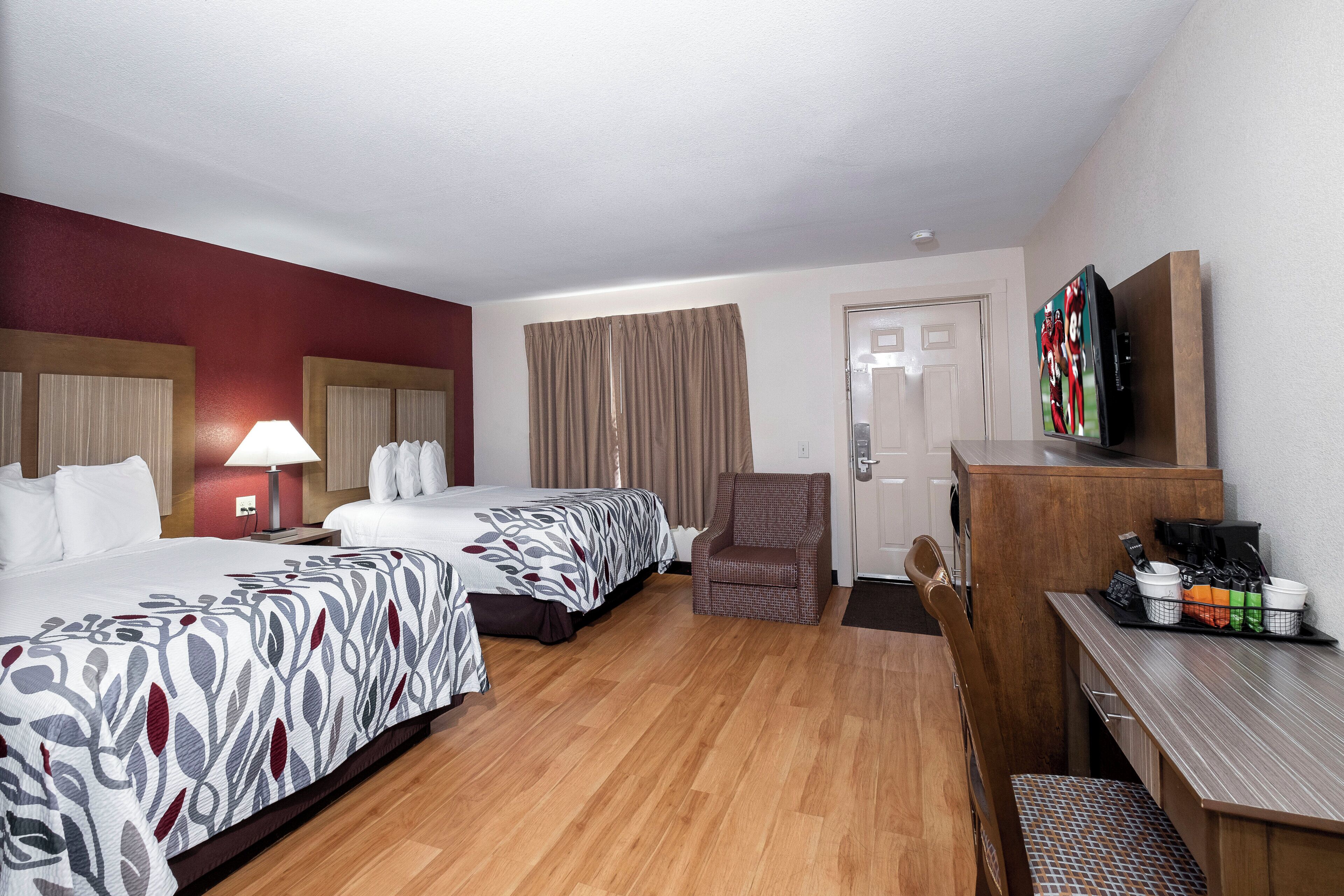 Una habitación de hotel con dos camas, un escritorio, una silla, un televisor y una cafetera.