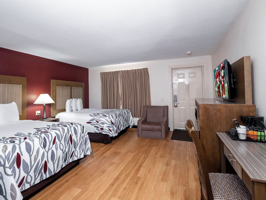 A hotel room with two beds, a desk, a chair, a television, and a coffee machine.