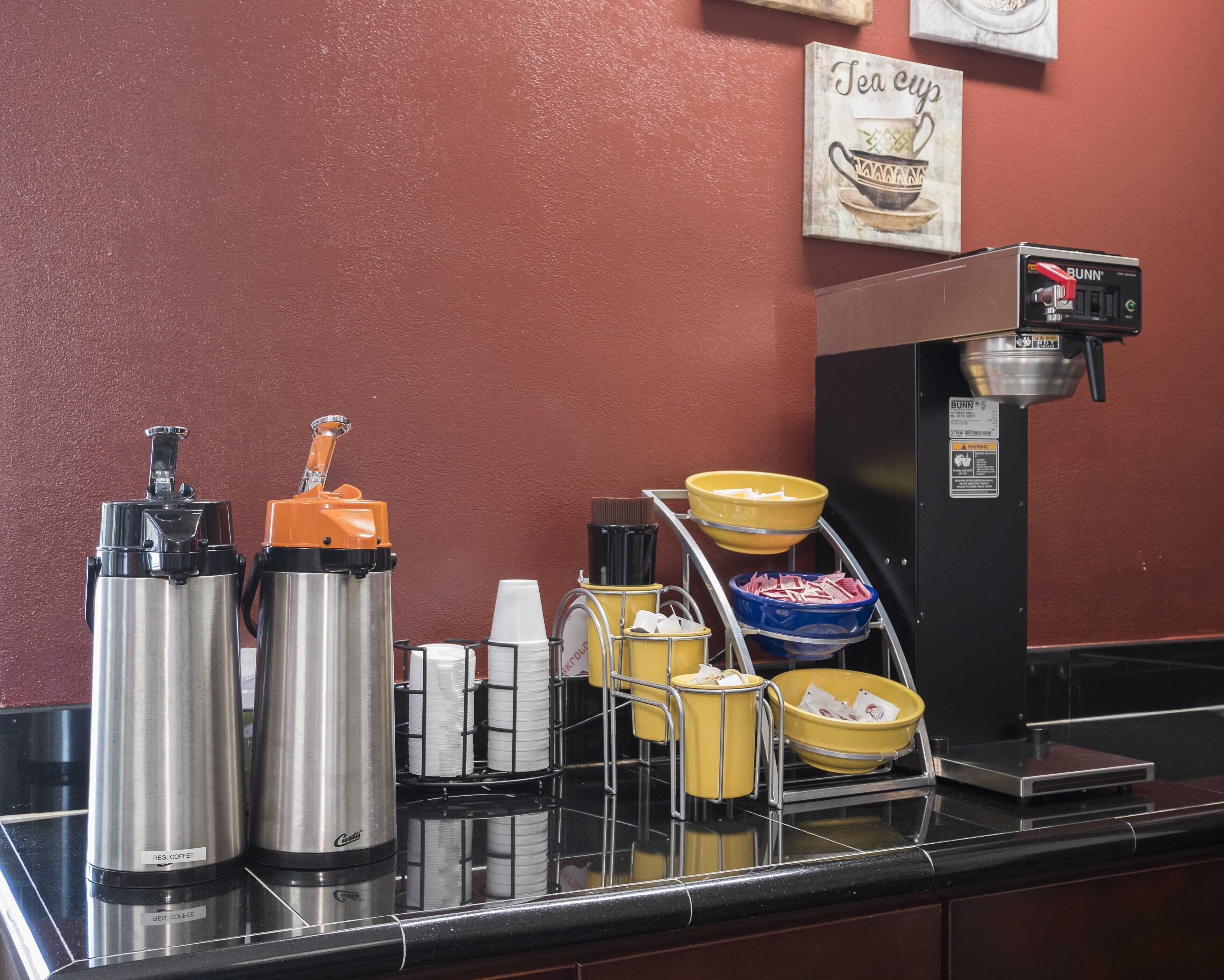 Un espace dédié au café, équipé d’une machine à café Bunn, de deux distributeurs de café en acier inoxydable et de différents récipients pour les gobelets et les serviettes.