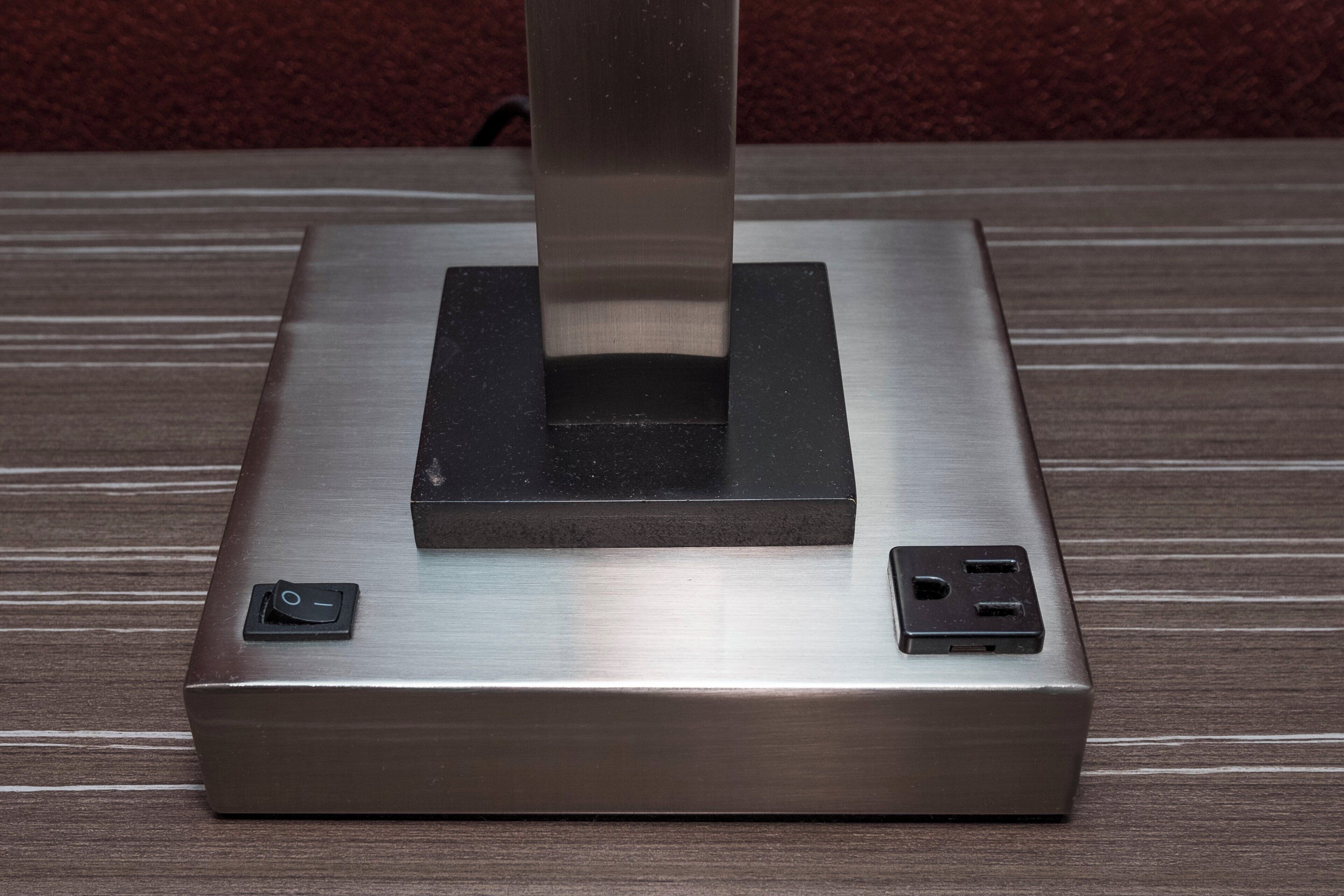 Objeto metálico con base cuadrada, una sección central sobresaliente y dos componentes rectangulares a los lados.