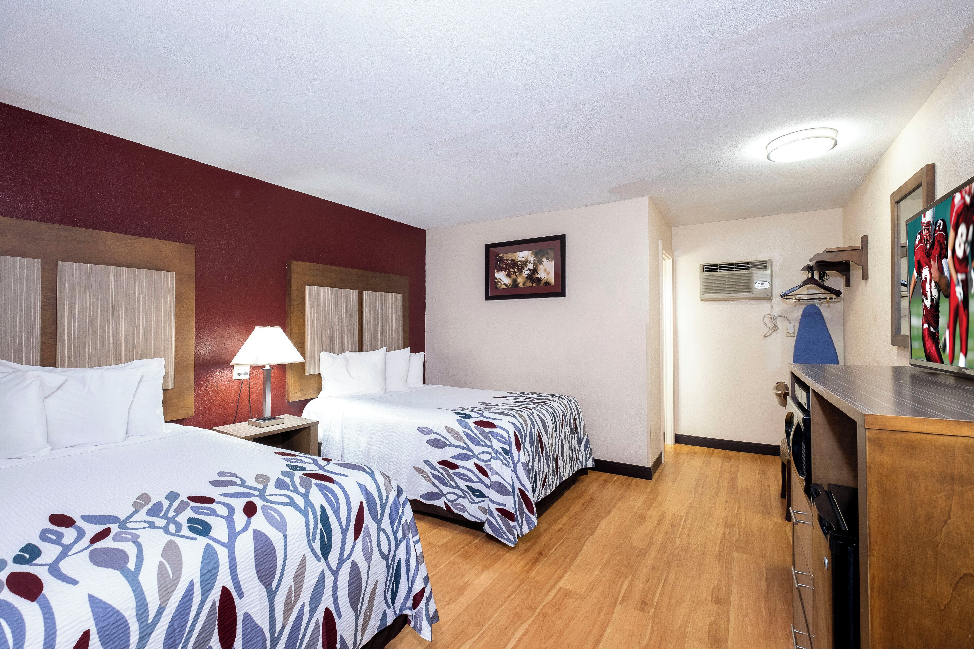 Une chambre d’hôtel avec deux lits, un bureau, une lampe, un tableau encadré, un climatiseur et un téléviseur.