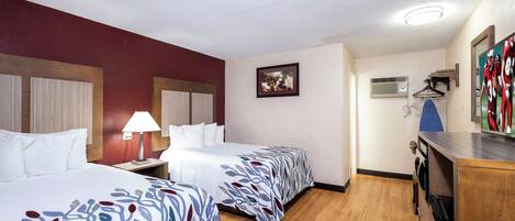 Une chambre d’hôtel avec deux lits, un bureau, une lampe, un tableau encadré, un climatiseur et un téléviseur.