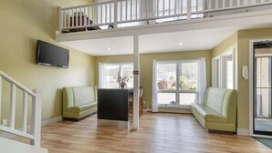A spacious living area with a wooden floor, a sofa, a television mounted on the wall, and a balcony with a railing.