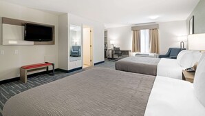Habitación de hotel con dos camas, un televisor montado en la pared, un escritorio con una silla y una ventana con cortinas.