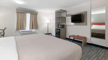Una habitación de hotel con una cama grande, un televisor de pantalla plana montado en la pared, un microondas y una mesita con cubierta roja.