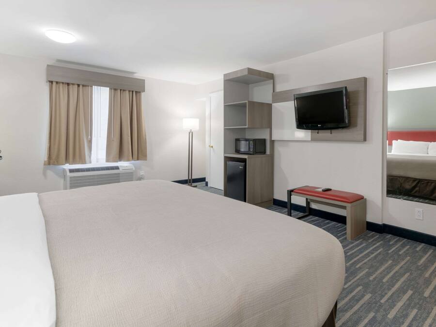 Una habitación de hotel con una cama grande, un televisor de pantalla plana montado en la pared, un microondas y una mesita con cubierta roja.