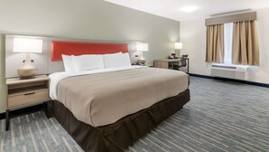 A hotel room with a large bed, two bedside tables with lamps, a window with curtains, and a wall-mounted air conditioning unit.