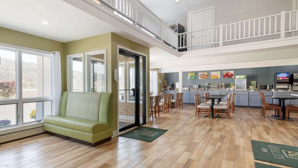 Amplia sala de estar con un sofá verde, comedor con sillas de madera, cocina con mostrador y balcón con barandilla.