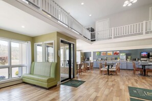 A spacious living area with a green sofa, a dining area with wooden chairs, a kitchen with a counter, and a balcony with a railing.
