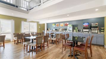 A spacious dining area with multiple tables and chairs, a kitchen area with appliances, and a staircase leading to an upper level.