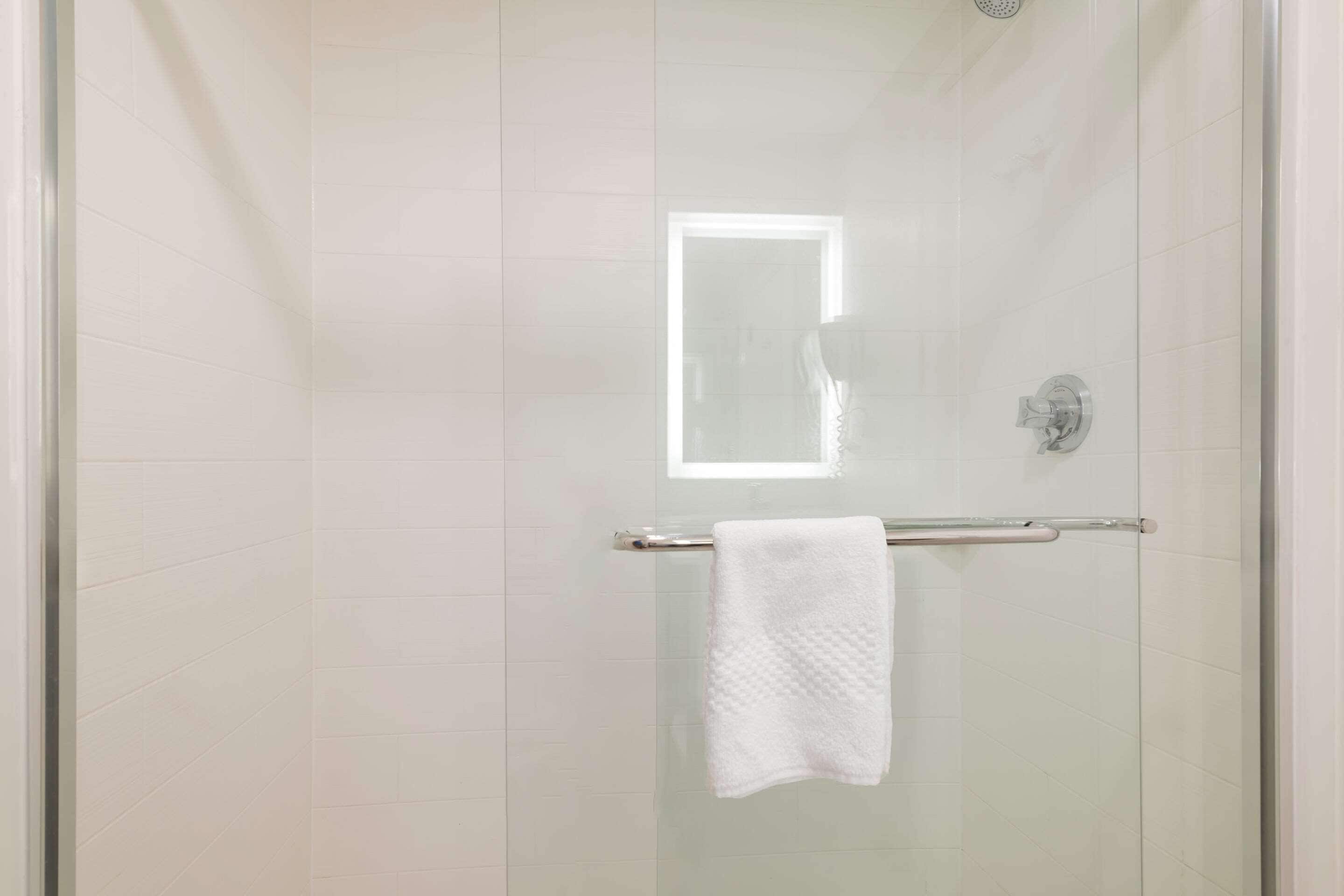 Ducha envuelta en vidrio con una toalla blanca colgada en una barra de metal.
