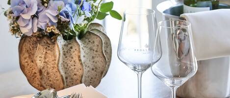A dining table set with plates, cutlery, and wine glasses, a vase with flowers, and a bottle of wine.