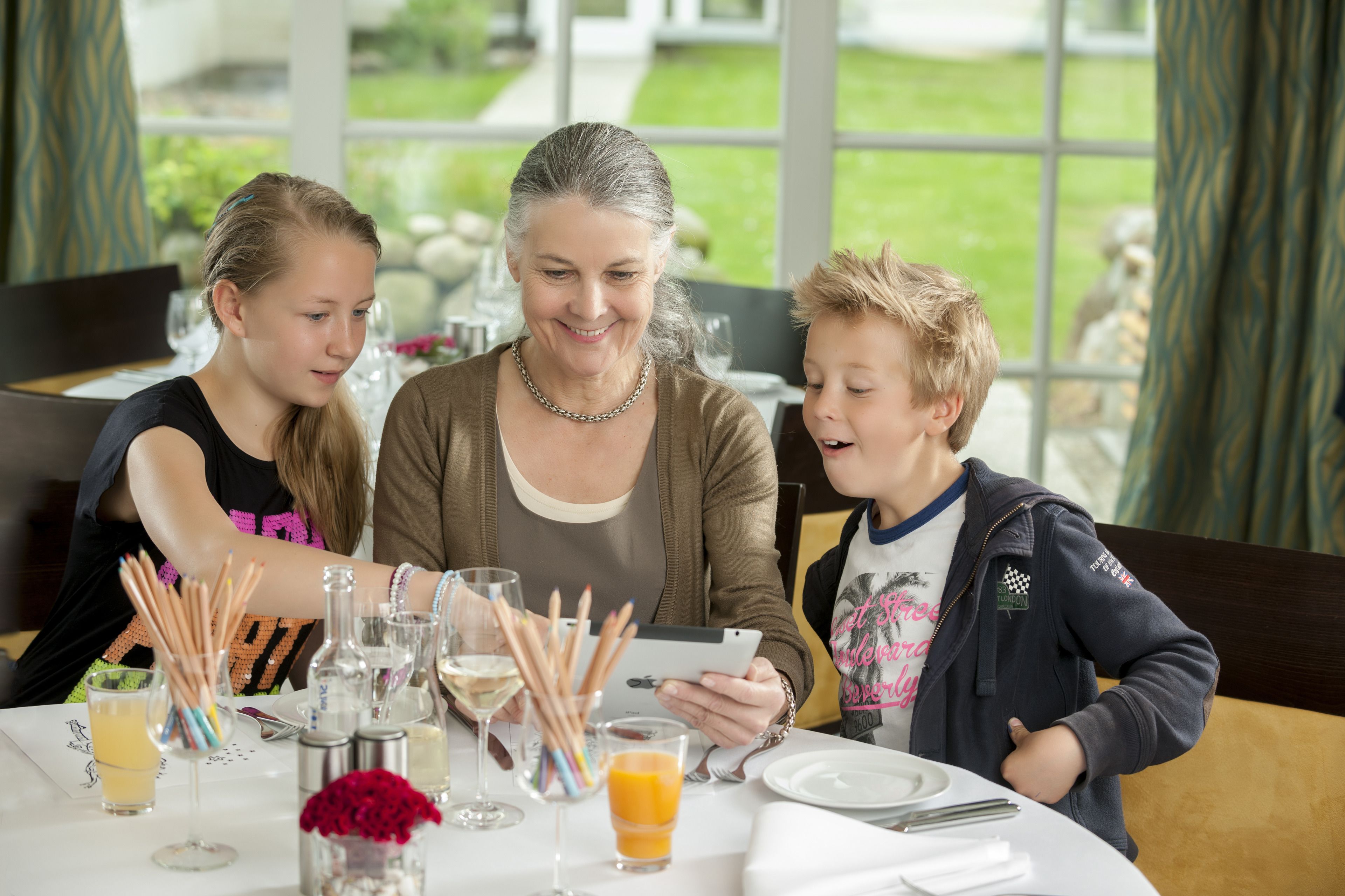 Una mesa de comedor con una familia de tres personas, una tableta y diversos objetos como vasos y una botella.