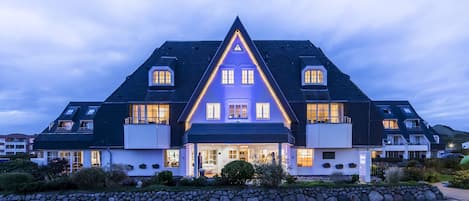 A large, modern house with a steeply pitched roof, multiple windows, and a well-lit entrance.