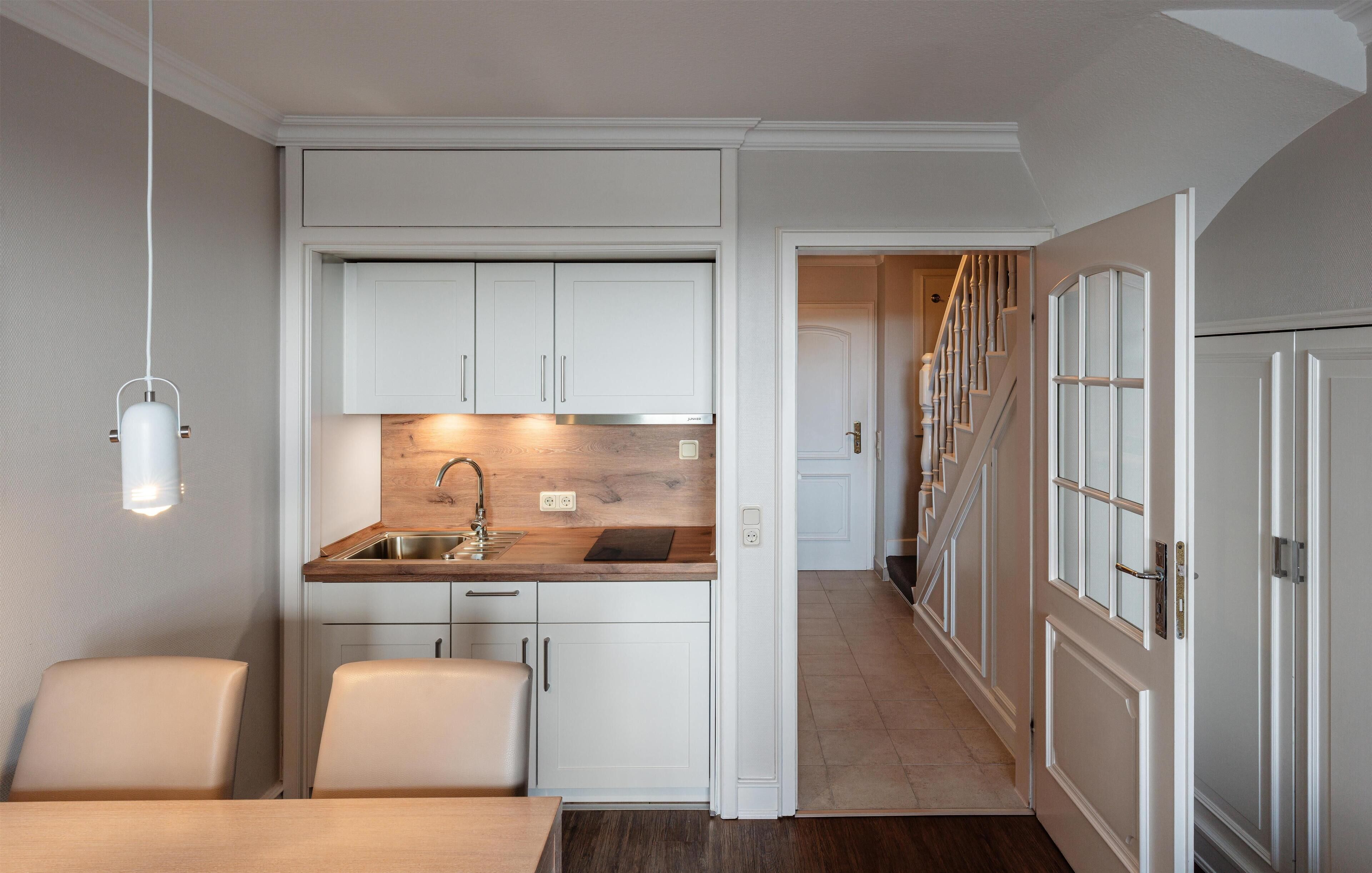 A compact kitchen with white cabinetry, a wooden countertop, and a built-in sink. There is a dining area with a table and chairs, and a staircase leading to another level.