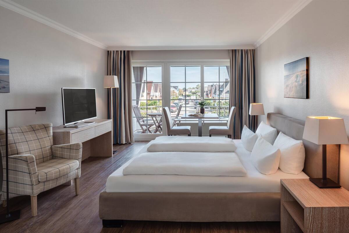 Et hotelværelse med en seng, et skrivebord med et fjernsyn, en stol, et bord med stole og udsigt ud.