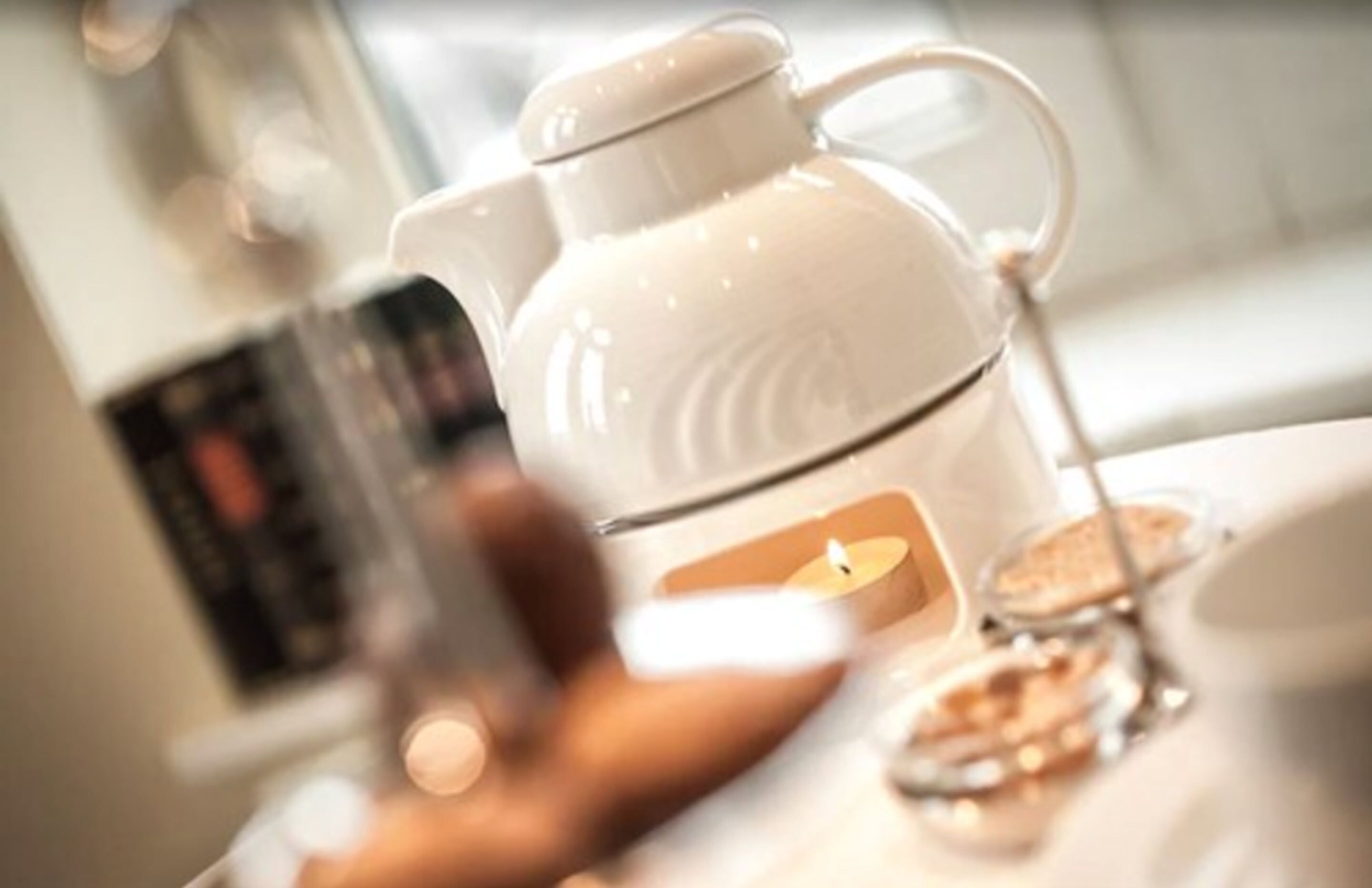 A teapot on a table with a candle and a glass.