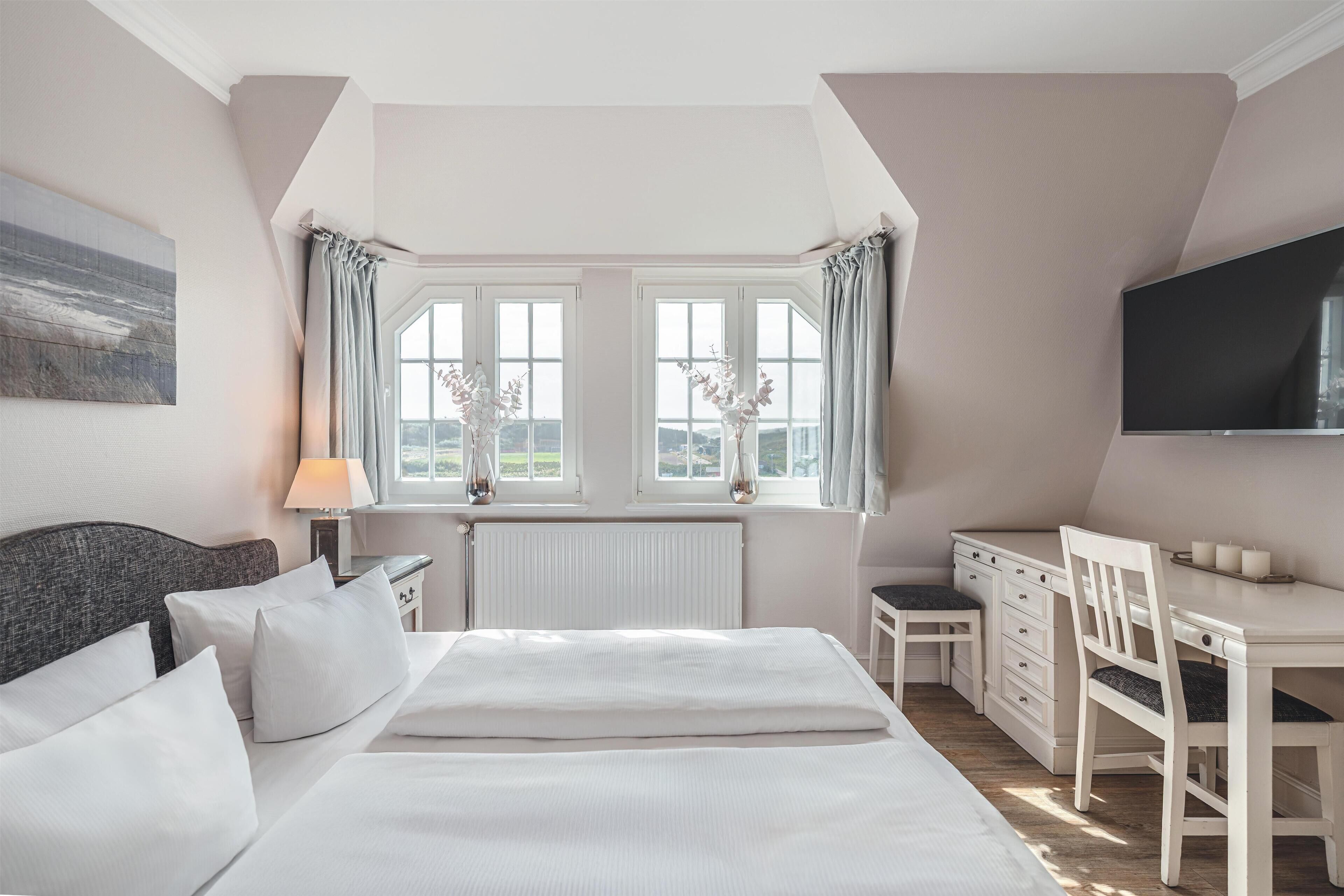 A bedroom with a large bed, a desk, and a TV.