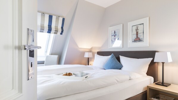 A hotel room with a bed, bedside tables, a window with curtains, and two framed pictures on the wall.