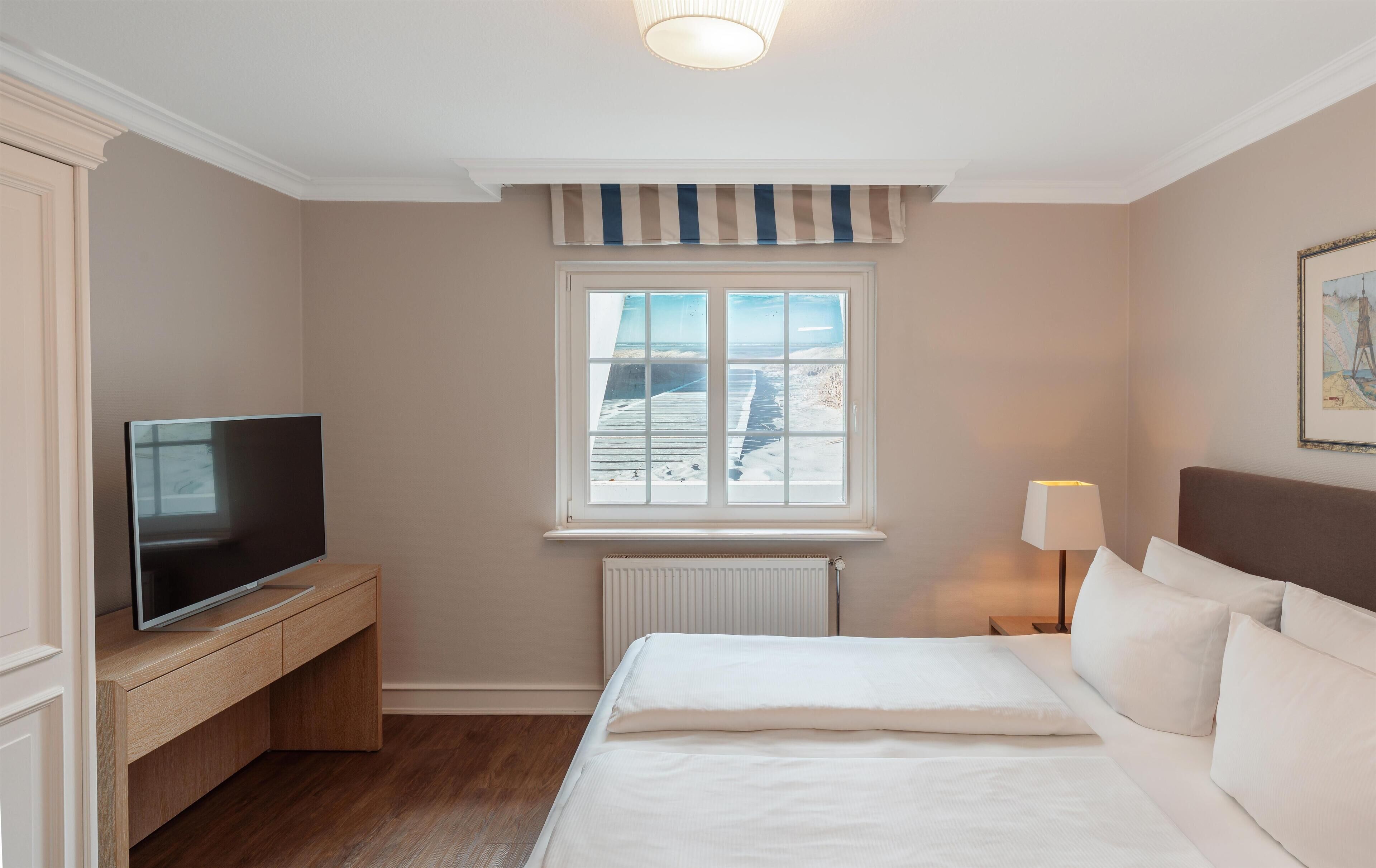 A hotel room with a bed, a TV, a window with a view of the beach, and a lamp.