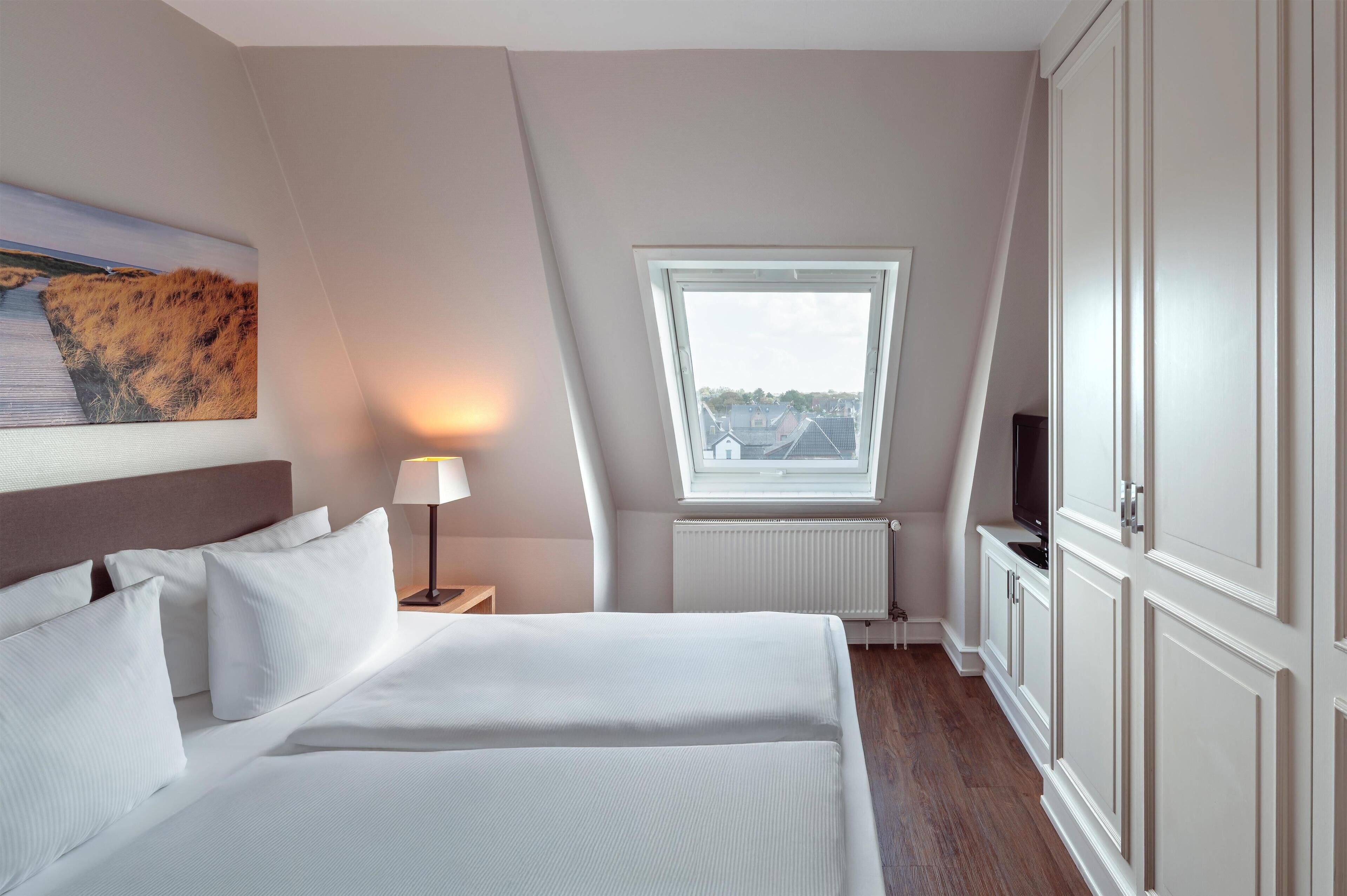 Una habitación de hotel con una cama, televisión, ventana y un cuadro en la pared.
