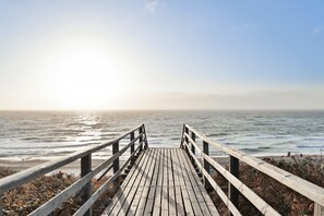 A wooden pier leading to a beach with the ocean in the background.