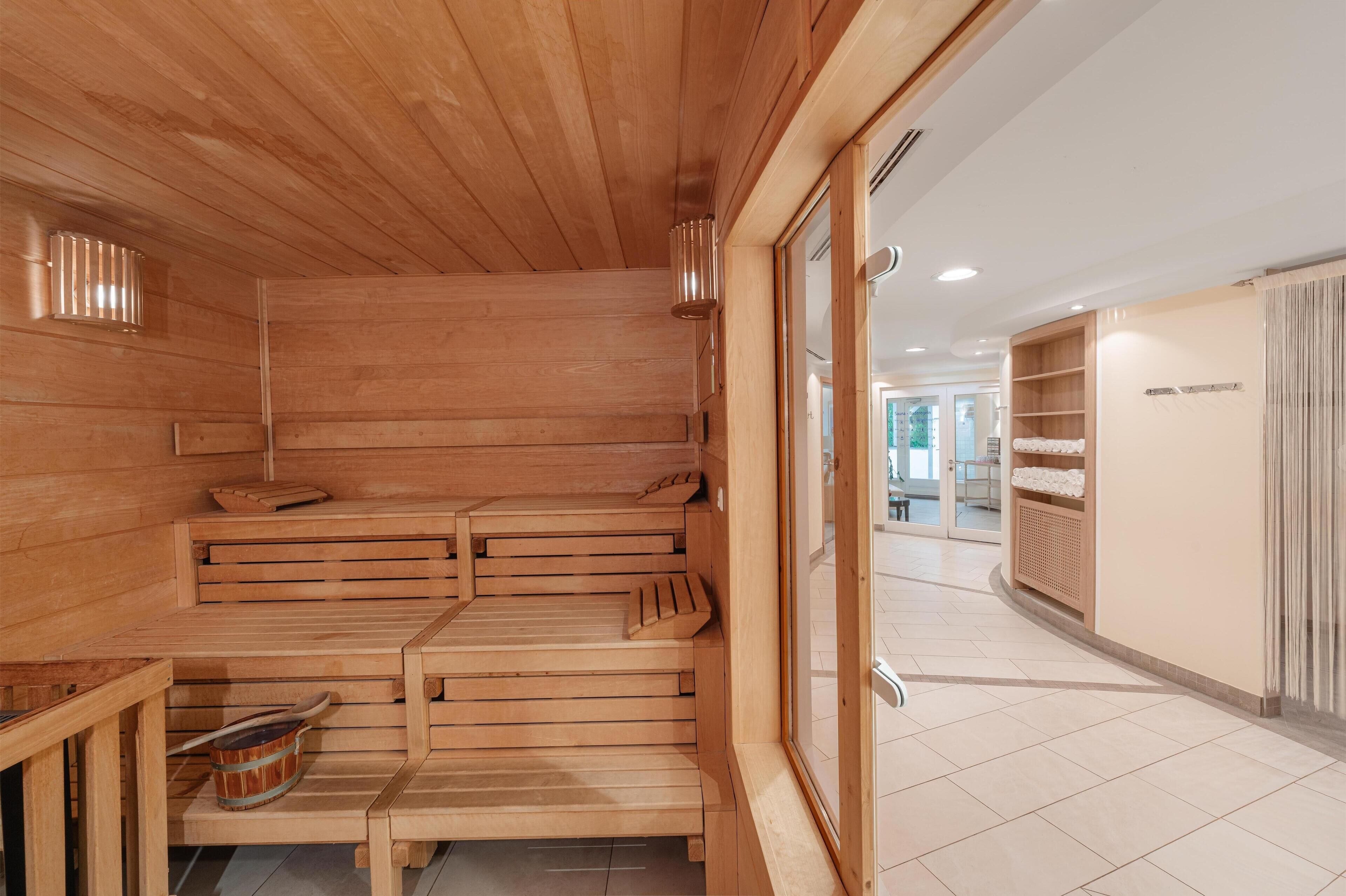 A wooden sauna with benches and a small table, a towel rack, and a window to the outside.