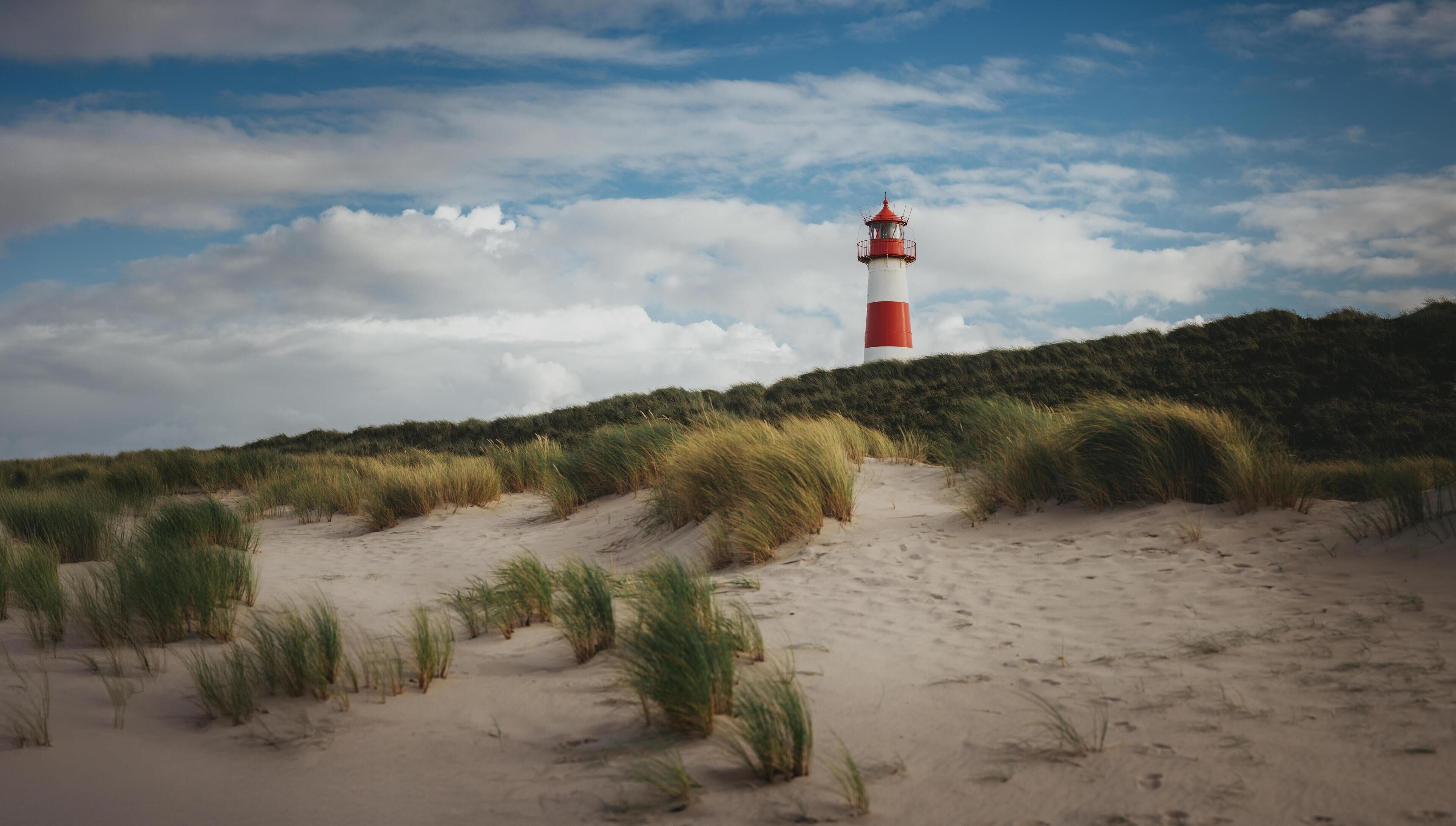A lighthouse on a sandy dune with grass in the foreground.