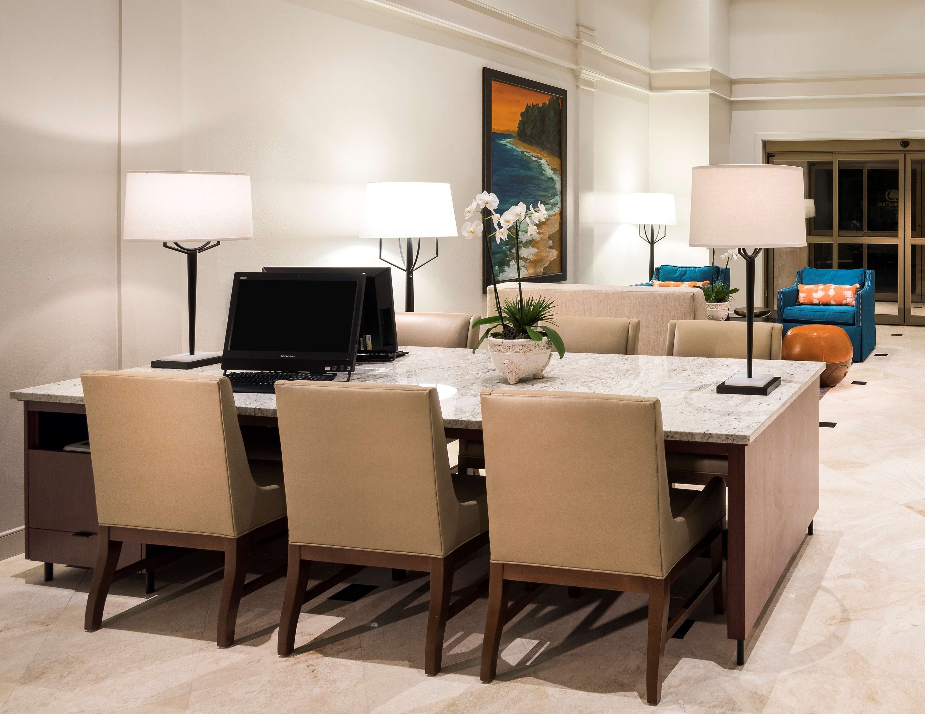 A dining area with a marble table, four chairs, two computer monitors, and a potted plant.