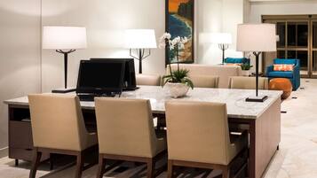 A dining area with a marble table, four chairs, two computer monitors, and a potted plant.