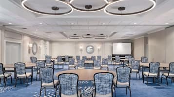 A conference room with round tables and chairs, a large screen, and circular ceiling lights.