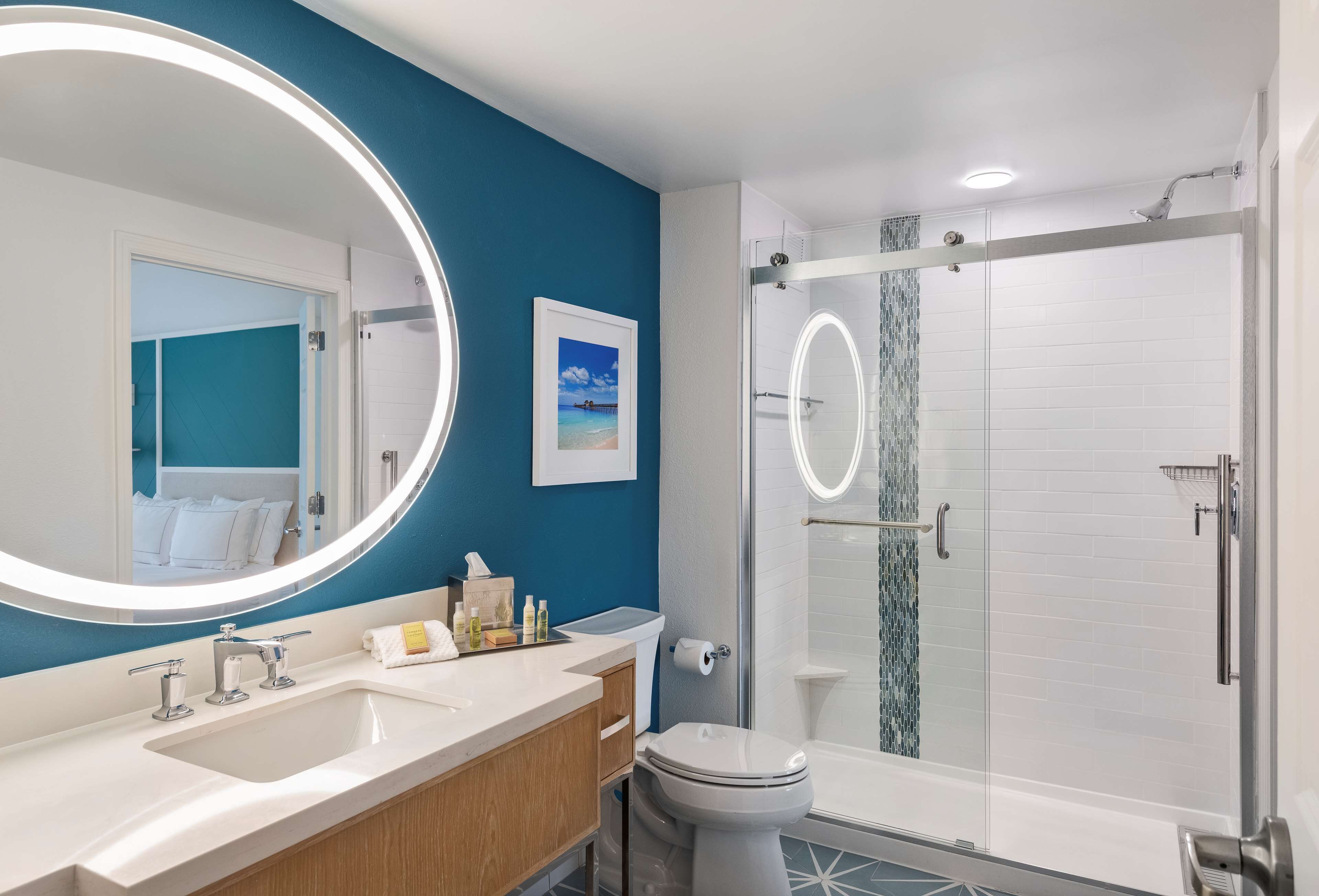 A modern bathroom with a large mirror, dual sinks, a toilet, and a glass-enclosed shower.