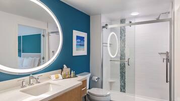 A modern bathroom with a large mirror, dual sinks, a toilet, and a glass-enclosed shower.