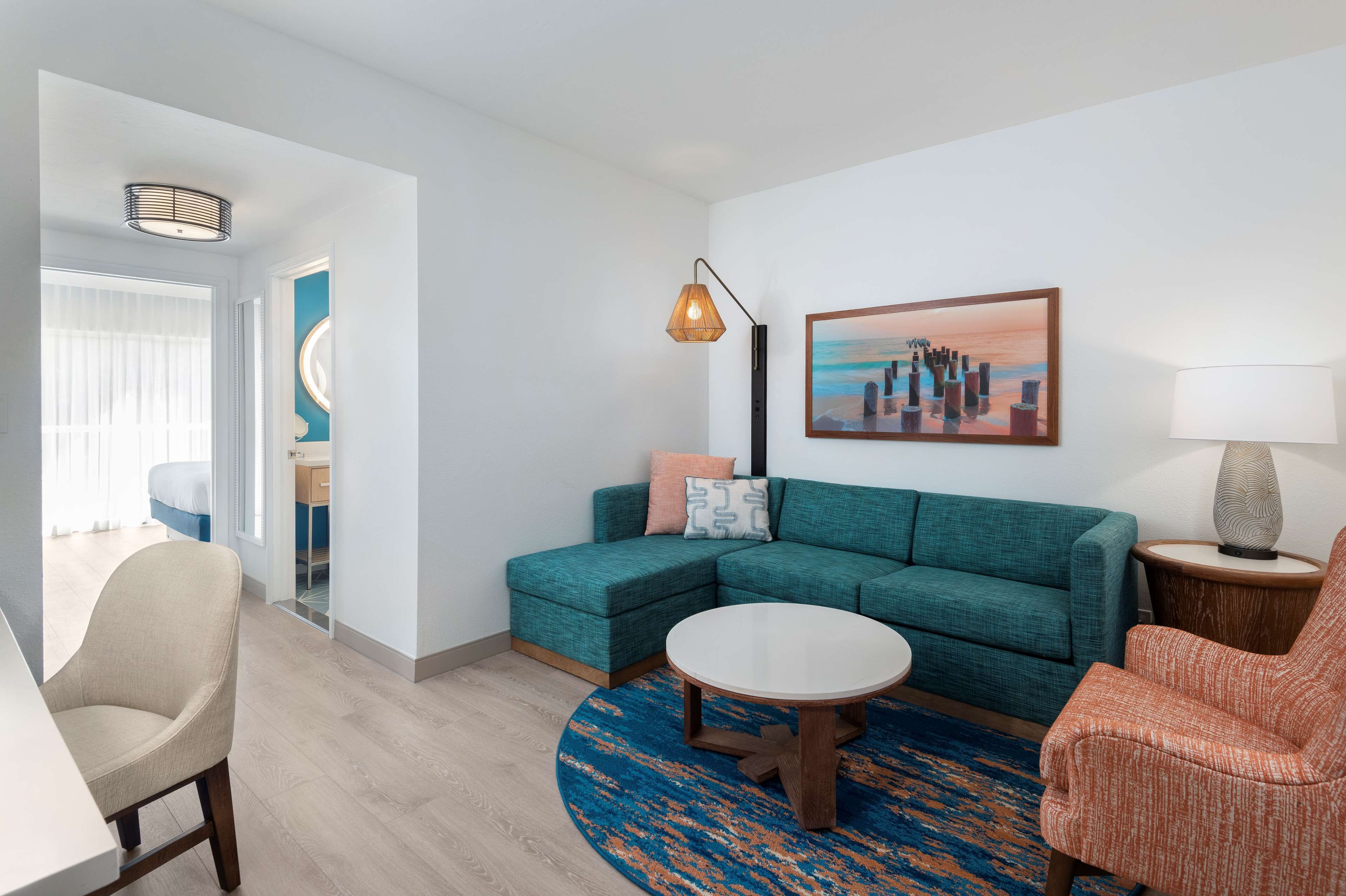 A modern living room with a teal sectional sofa, a round coffee table, and a blue patterned rug.