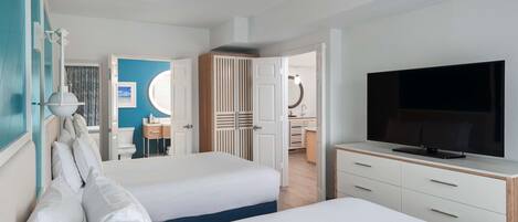 A hotel room with two beds, a TV, a desk, and a bathroom visible through an open door.