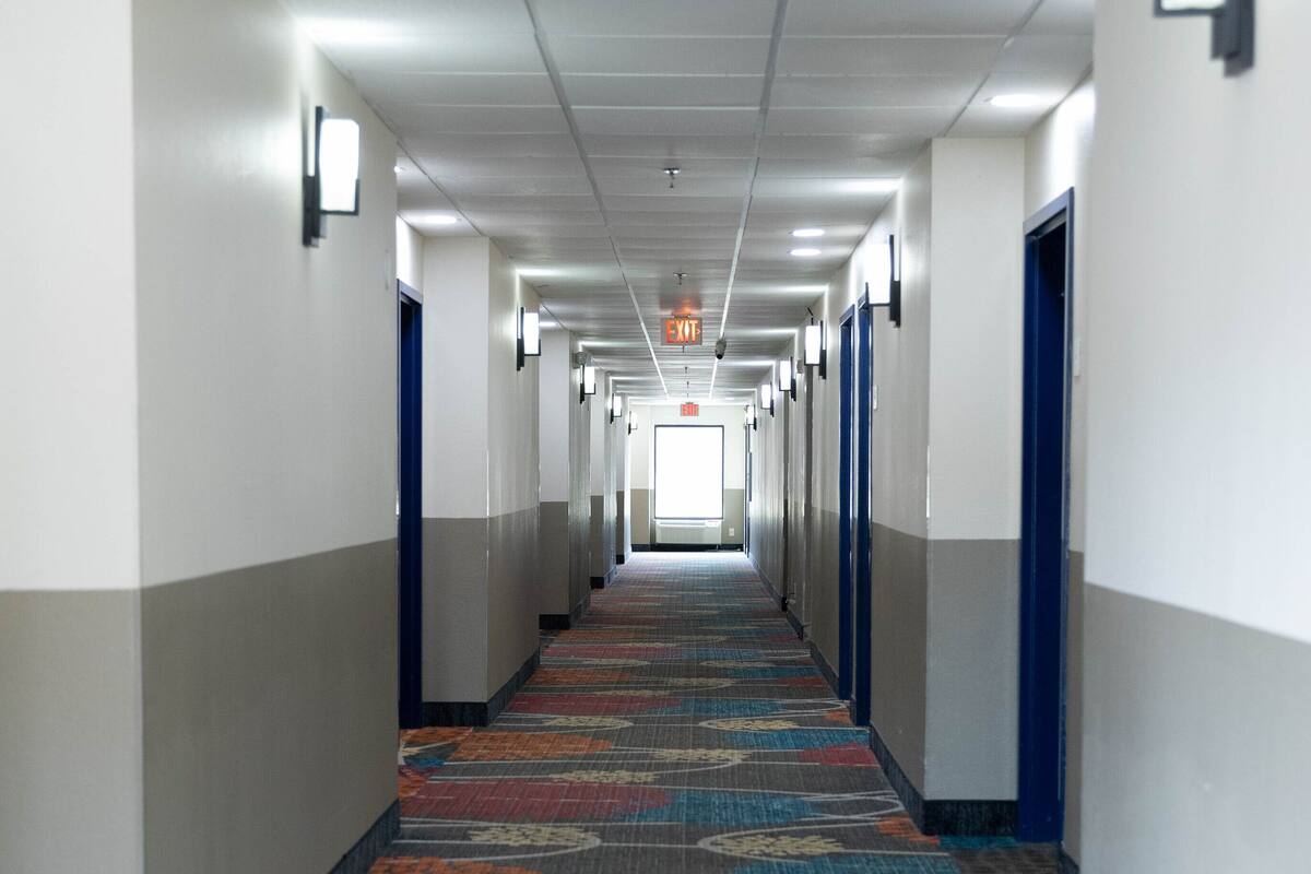 Un largo y estrecho pasillo de hotel con alfombra estampada, paredes blancas y puertas azules.