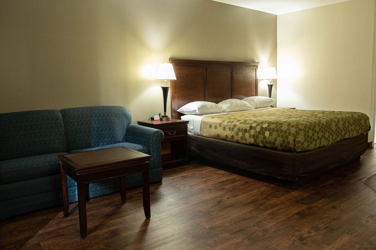Una habitación de hotel con una cama, un sofá azul, una mesita de noche de madera y dos lámparas.