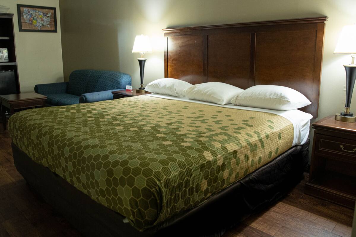 Habitación de hotel con una cama grande, dos lámparas de noche, un cabecero de madera, un sillón azul, una mesita y un mueble con microondas.