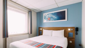 A hotel room with a large bed, a wooden headboard, a bedside table with a lamp, a wall-mounted phone, and a window with curtains. - Travelodge Belfast Central (Belfast)